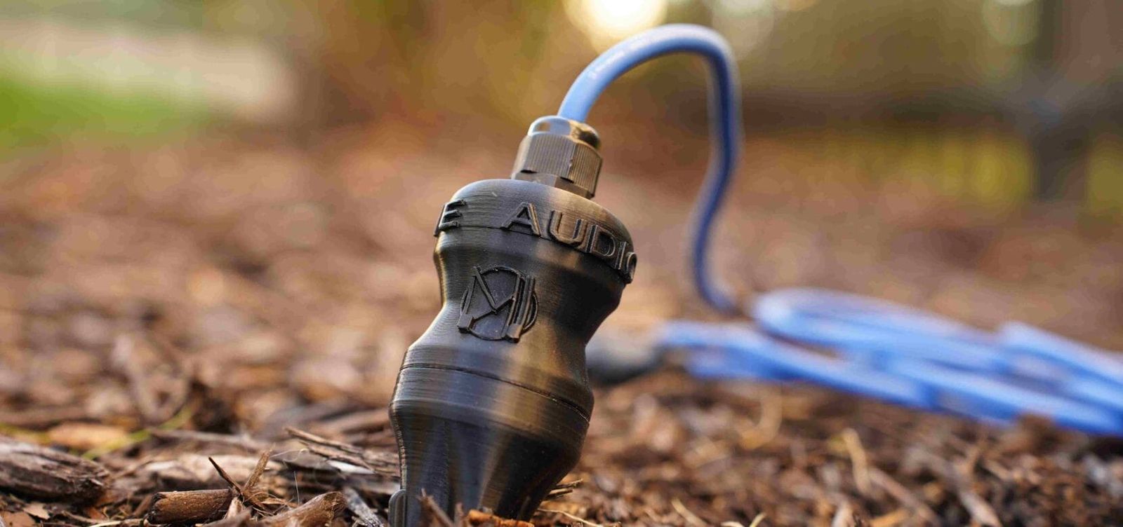 Géophone Manalive Audio posé sur un sol forestier, câble bleu